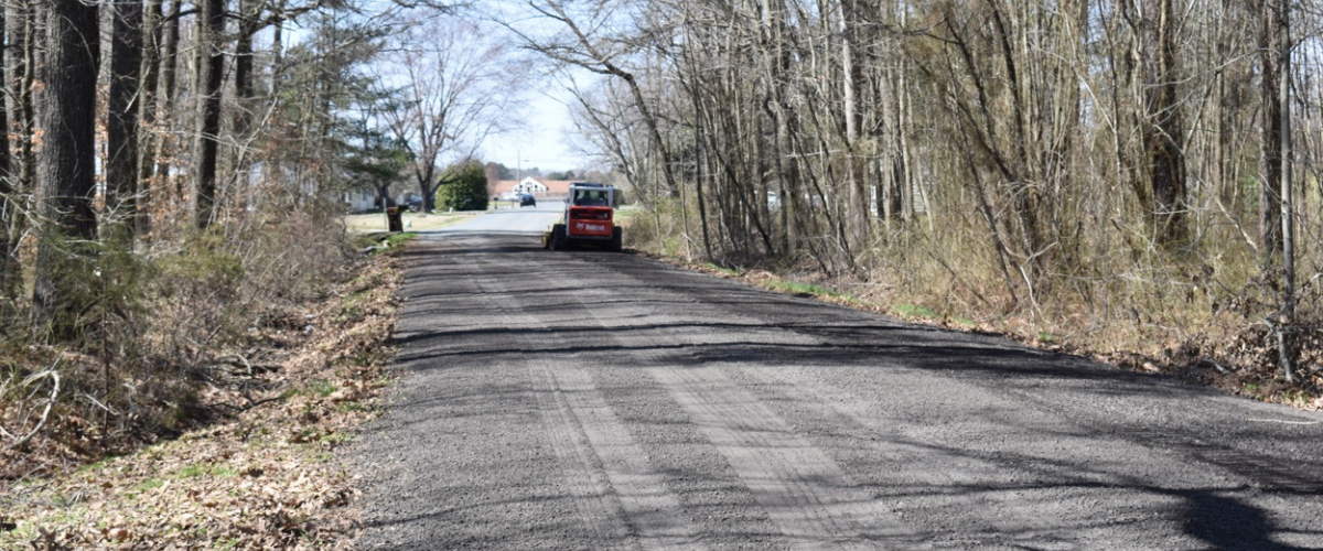 gravel driveway sitting between two lines of trees with skid steer loader in the distance