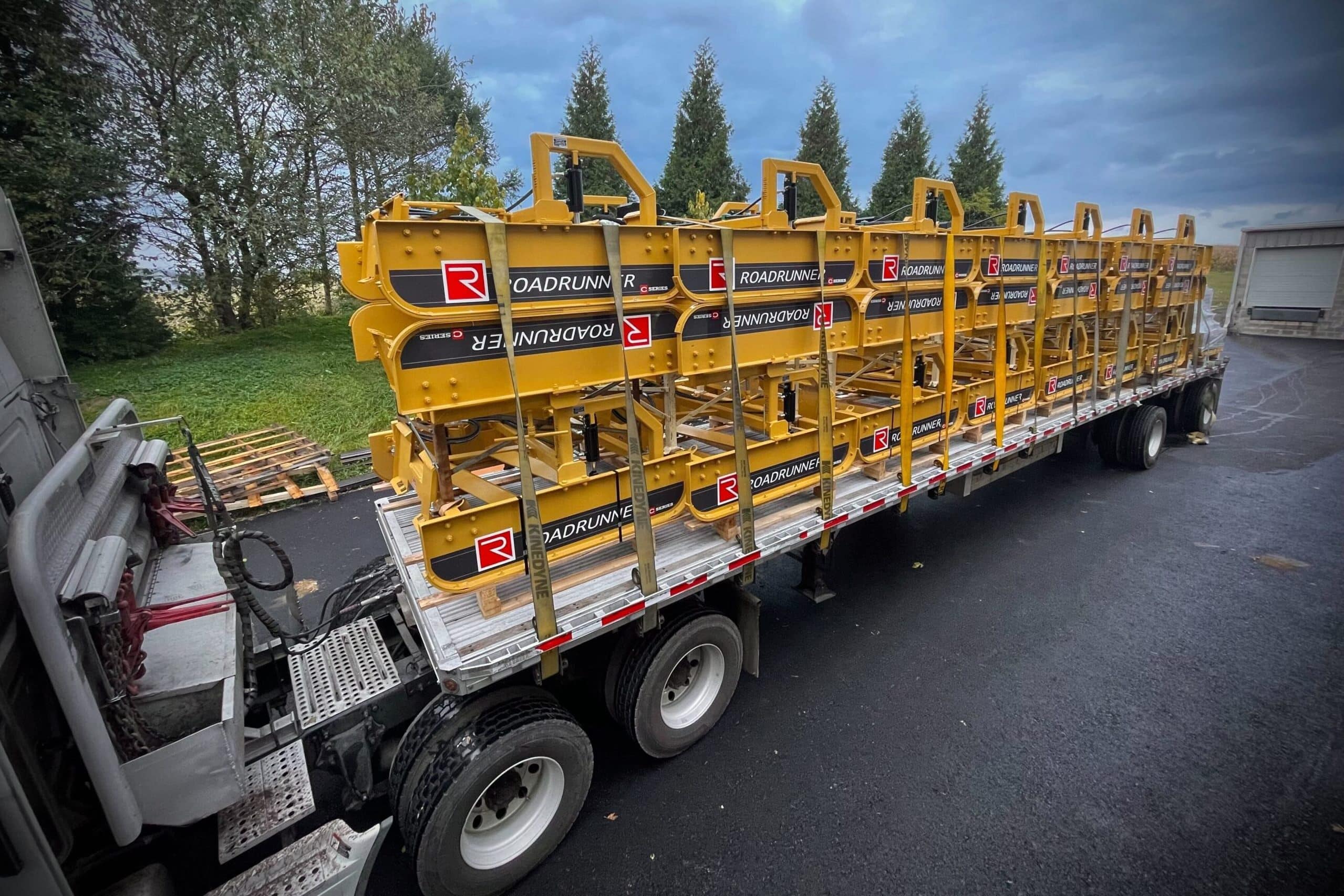 Compact tractor with Roadrunner grader blade smoothing a gravel road, showcasing dual blades, rugged steel frame, and precise grading action